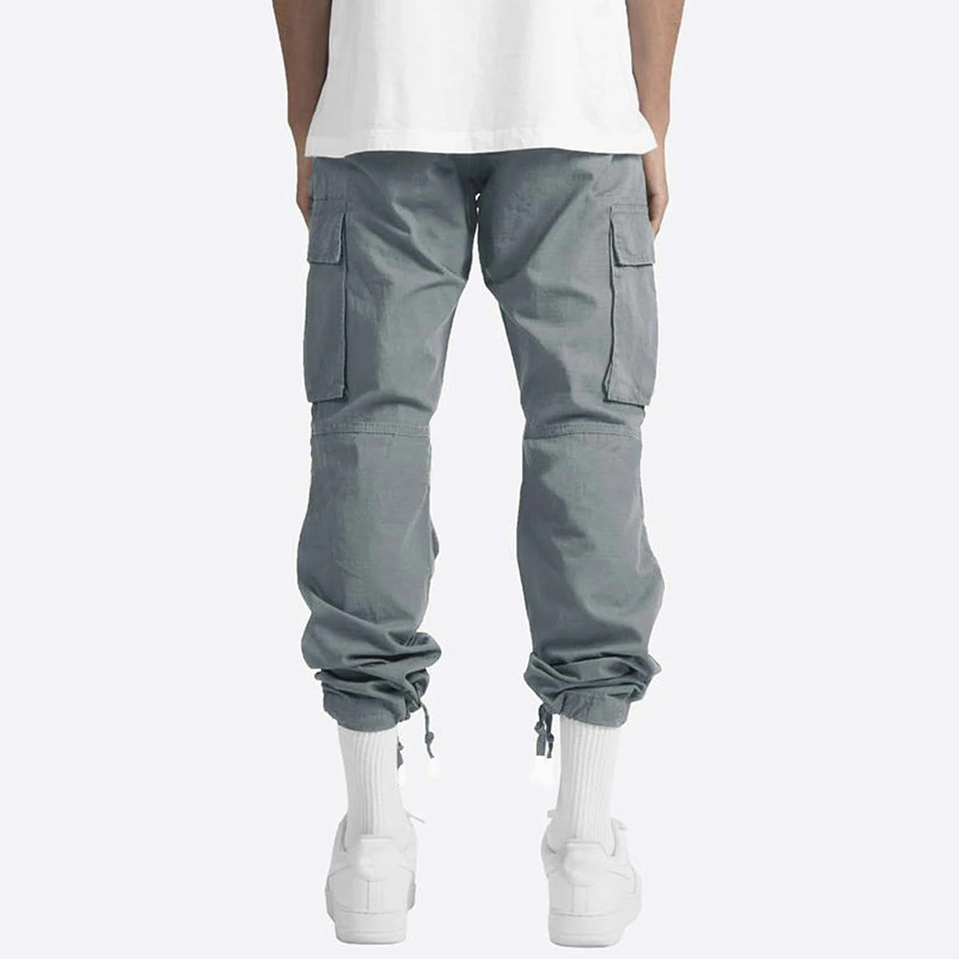 Grijze cargobroek voor heren, Ryker model, met zakken en elastische boorden, gedragen met witte sneakers en sokken.