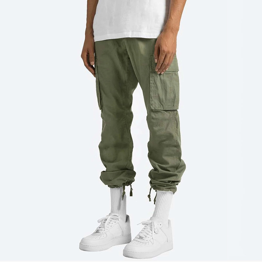 Groene cargobroek voor heren met zakken, gedragen met witte sneakers en sokken. Ideaal voor casual streetwear en outdoor activiteiten.