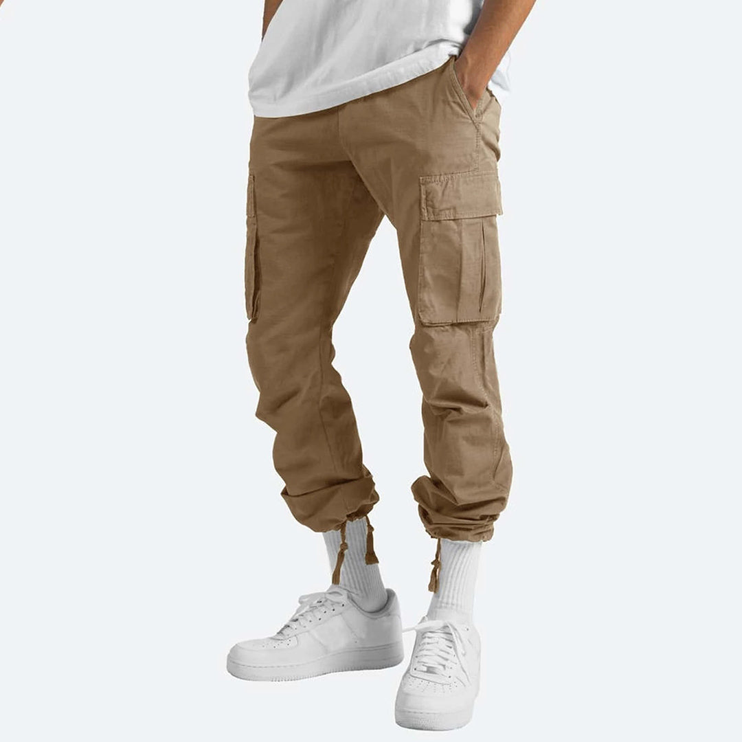 Beige cargobroek voor heren met zakken, casual stijl, gecombineerd met witte sneakers en sokken. Comfortabele en modieuze broek voor dagelijks gebruik.