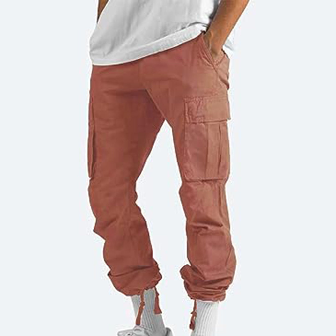 Bruine cargobroek voor heren, met meerdere zakken en elastische boorden, gedragen met witte sneakers. Comfortabele en modieuze streetwear.