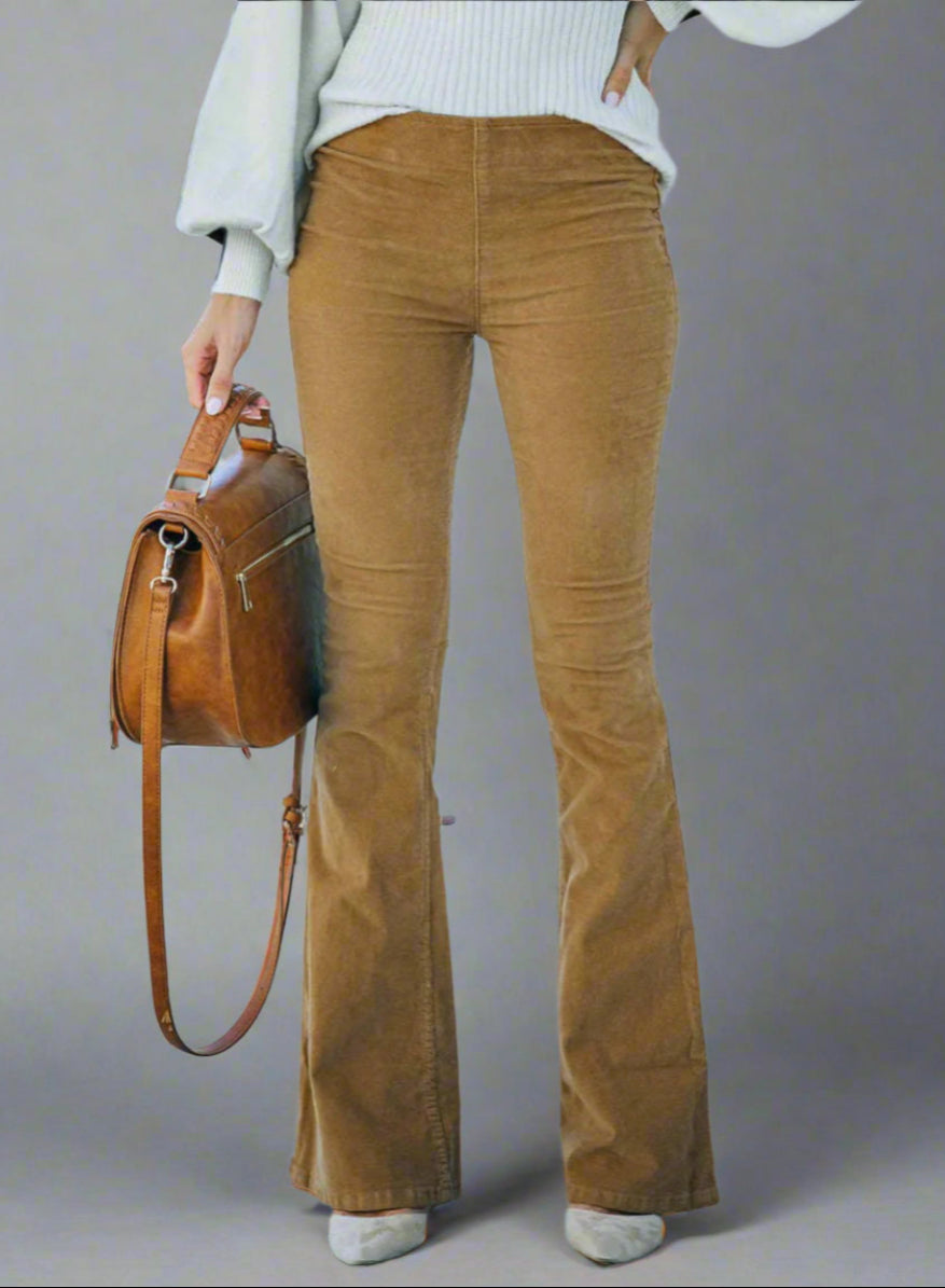 Vrouw draagt bruine flared broek met witte trui, houdt bruine leren tas vast. Modieuze herfstoutfit, casual stijl, trendy damesmode.