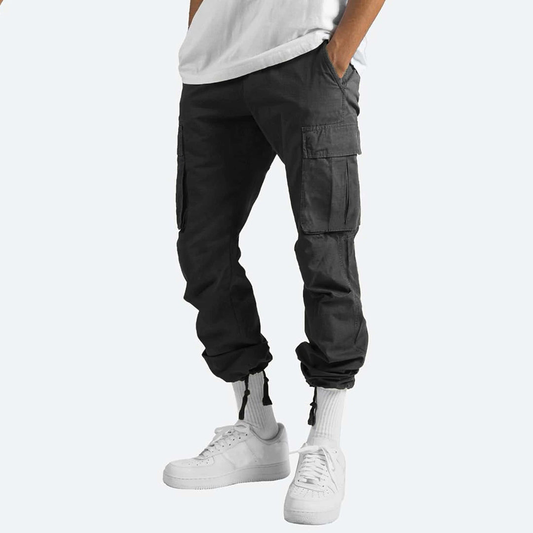 Zwarte cargobroek voor heren, met meerdere zakken en elastische boorden, gecombineerd met witte sneakers en een wit T-shirt.