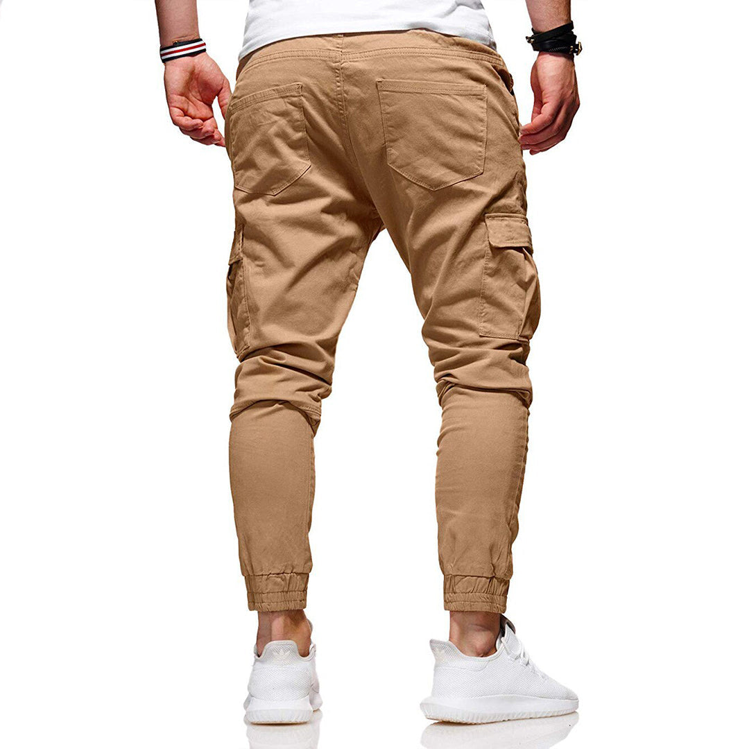 Man in beige cargobroek, achteraanzicht, met elastische enkels en zakken, casual stijl, gecombineerd met witte sneakers en een wit T-shirt.